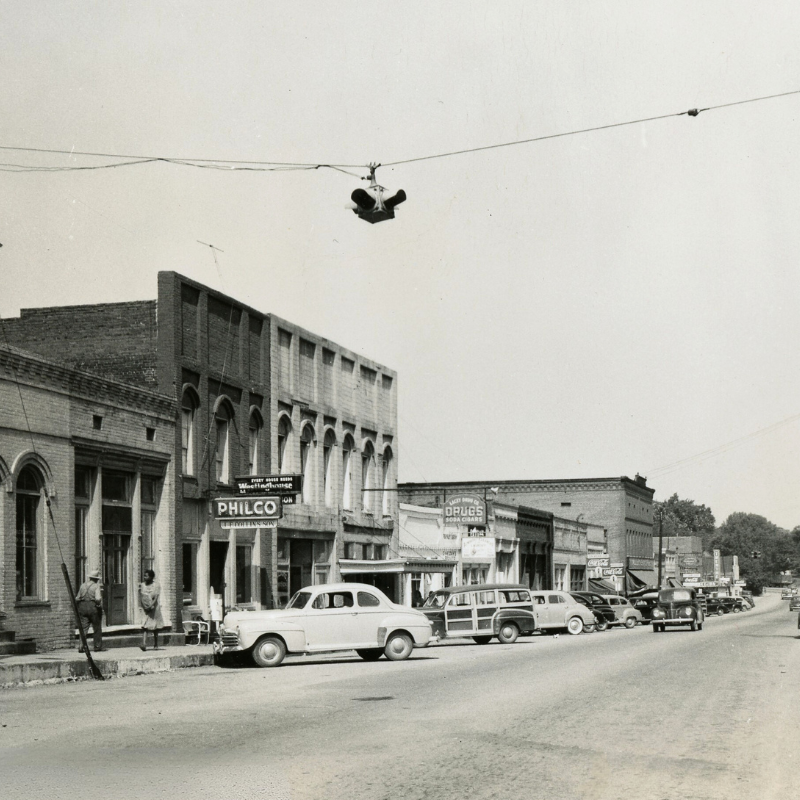Black-and-white photo of a small town street with parked vintage cars, brick storefronts, and a traffic signal suspended overhead. Learn more about historic Acworth locations captured in timeless moments like this. Black-and-white photo of a small town street with parked vintage cars, brick storefronts, and a traffic signal suspended overhead. Learn more about historic Acworth locations captured in timeless moments like this.