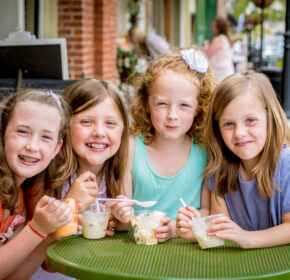 Four young girls sit at a green outdoor table, smiling and enjoying ice cream on a sunny day—one of the best ways to stay cool this summer in Acworth.