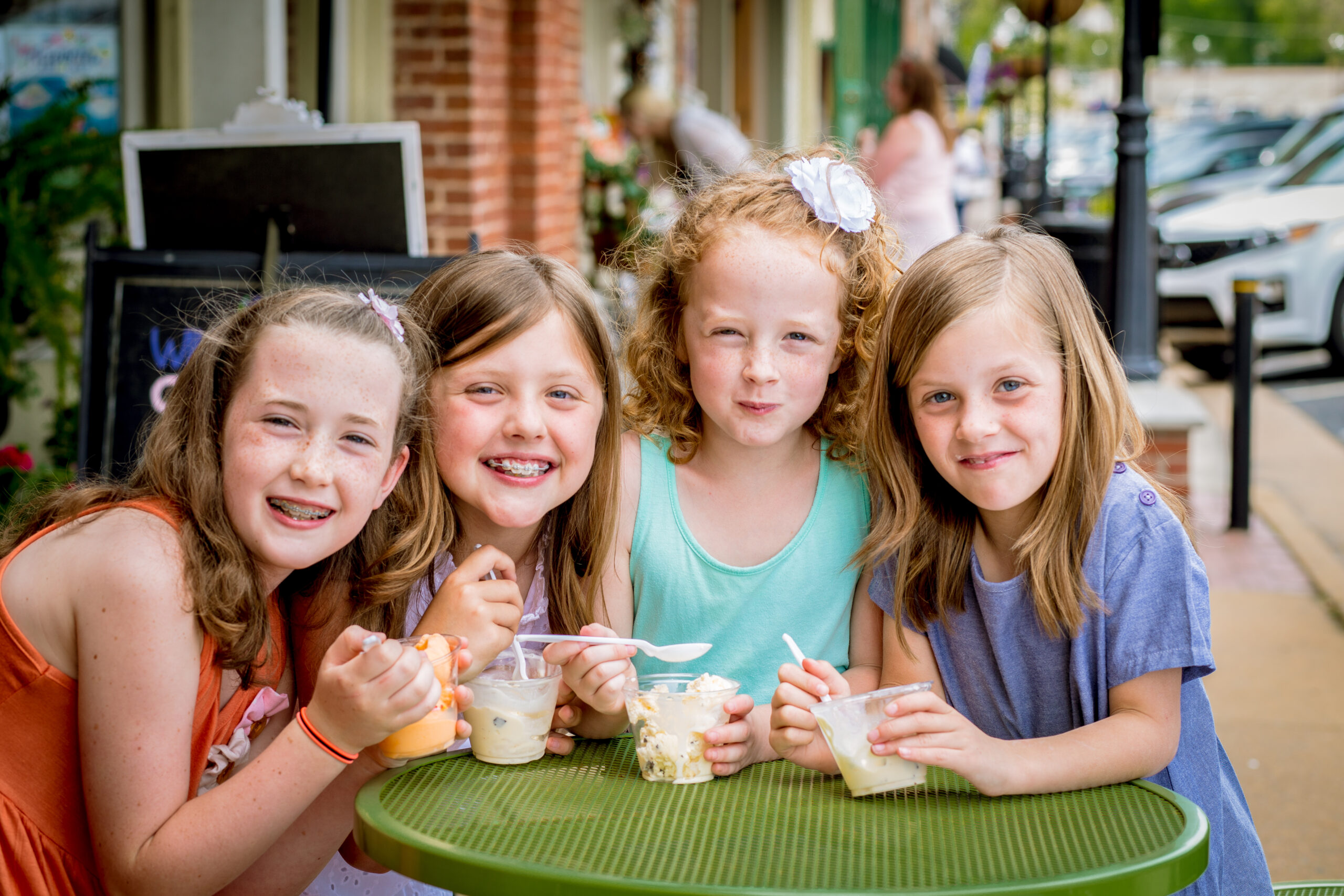 Four young girls sit at a green outdoor table, smiling and enjoying ice cream on a sunny day—one of the best ways to stay cool this summer in Acworth.