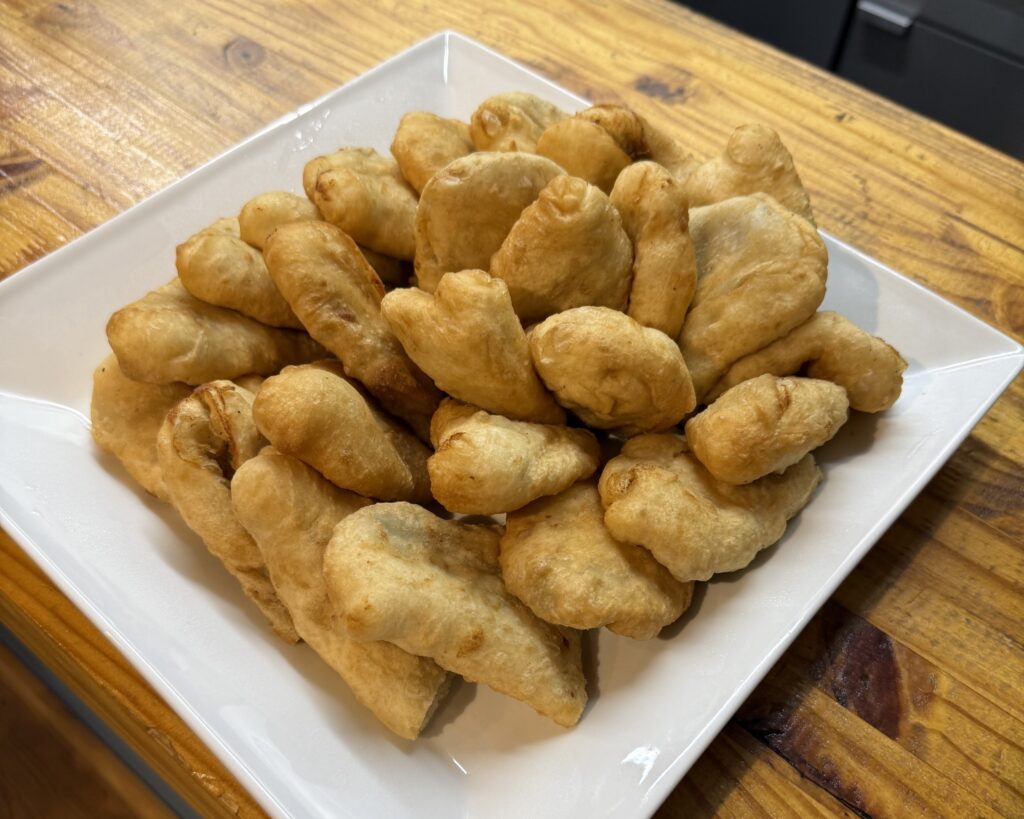 A white square plate filled with golden brown fried dough pieces sits on a wooden countertop.