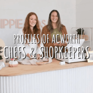 Two women stand behind a counter with a cash register and plants. Text overlay reads "Profiles of Acworth Chefs & Shopkeepers—Celebrate the Season in Acworth.
