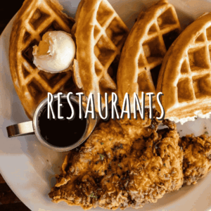 A plate with three waffle quarters, crispy fried chicken, a metal cup of syrup, and a scoop of butter on top—Celebrate the Season in Acworth with this delicious feast. The word "RESTAURANTS" is overlaid in large text.