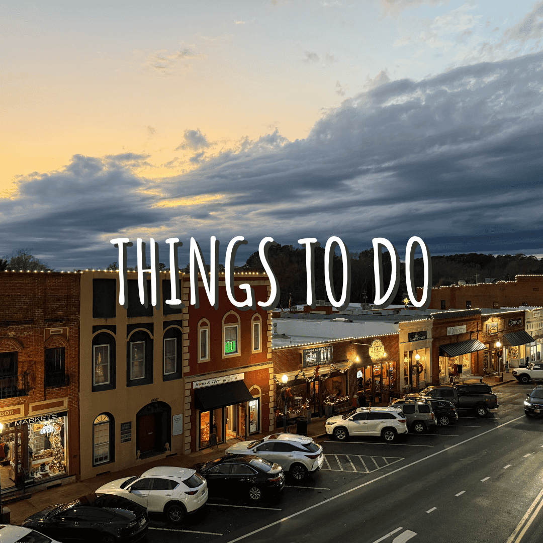 A small town main street in Acworth at sunset, with parked cars and brick buildings. Large text over the image reads “THINGS TO DO.” Celebrate the Season in Acworth.