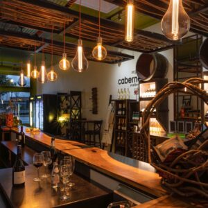 Modern wine bar interior with wooden counters, wine bottles, glasses, hanging light bulbs, and decorative wine barrels on the wall—stay cool in Acworth while enjoying a stylish atmosphere and exceptional wines.