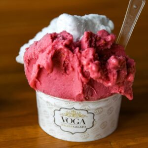 A cup of Voga Italian gelato with two flavors, one pink and one white, served with a small plastic spoon on a wooden surface—perfect to stay cool in Acworth.
