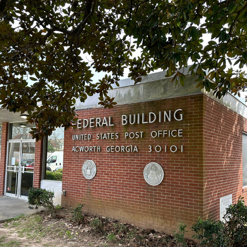 Red brick building with “Federal Building United States Post Office Acworth Georgia 30101” on the wall, two official seal plaques, and a glass entrance door visible on the left. Learn more about historic Acworth locations at this iconic site. Red brick building with "Federal Building United States Post Office Acworth Georgia 30101" on the wall, two official seal plaques, and a glass entrance door visible on the left. Learn more about historic Acworth locations at this iconic site.