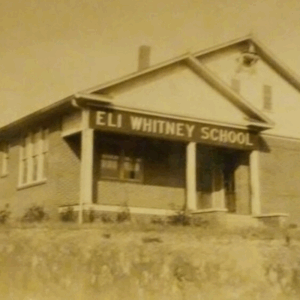Sepia-toned photo of a single-story brick building with a sign reading "Eli Whitney School" above the entrance. Discover its story and Learn More About Historic Acworth Locations.
