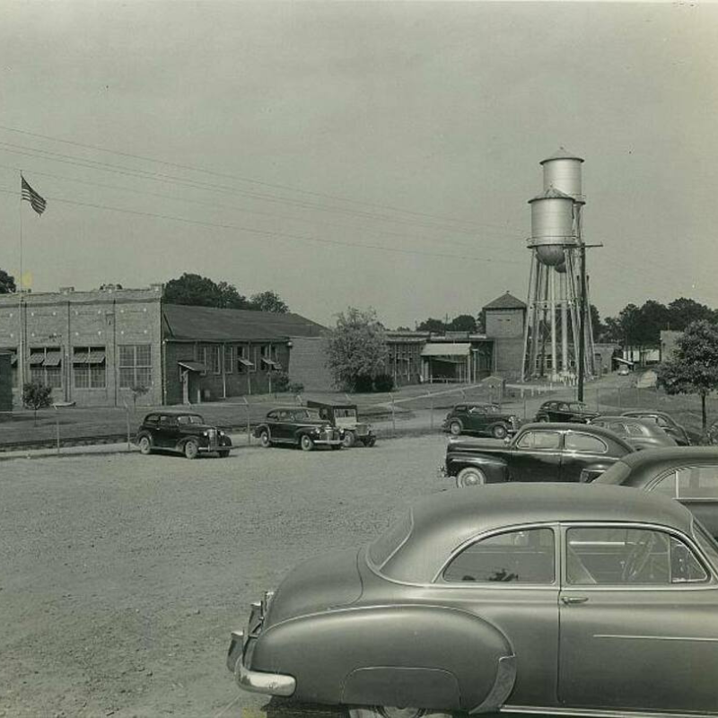 Black and white photo of vintage cars parked in a lot near industrial buildings and a tall water tower; an American flag is visible on the left. Learn more about historic Acworth locations captured in timeless moments like this. Black and white photo of vintage cars parked in a lot near industrial buildings and a tall water tower; an American flag is visible on the left. Learn more about historic Acworth locations captured in timeless moments like this.