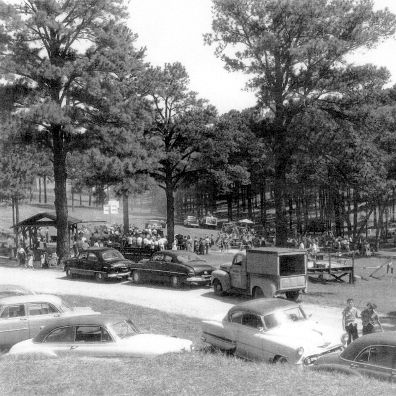Black-and-white photo of a park scene with vintage cars parked, people gathered near a pavilion, and tall trees in the background. Learn More About Historic Acworth Locations captured in this timeless moment. Black-and-white photo of a park scene with vintage cars parked, people gathered near a pavilion, and tall trees in the background. Learn More About Historic Acworth Locations captured in this timeless moment.