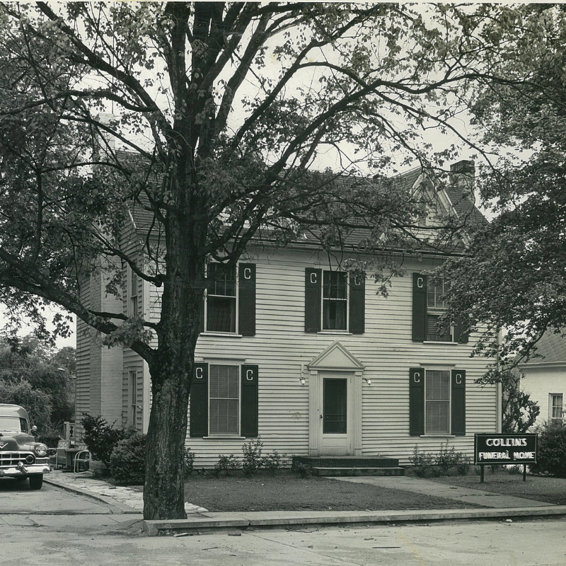 A two-story house with dark shutters and a large tree in front; a sign reads “Collins Funeral Home.” A vintage car is parked on the left. Learn More About Historic Acworth Locations at this fascinating landmark. A two-story house with dark shutters and a large tree in front; a sign reads “Collins Funeral Home.” A vintage car is parked on the left. Learn More About Historic Acworth Locations at this fascinating landmark.