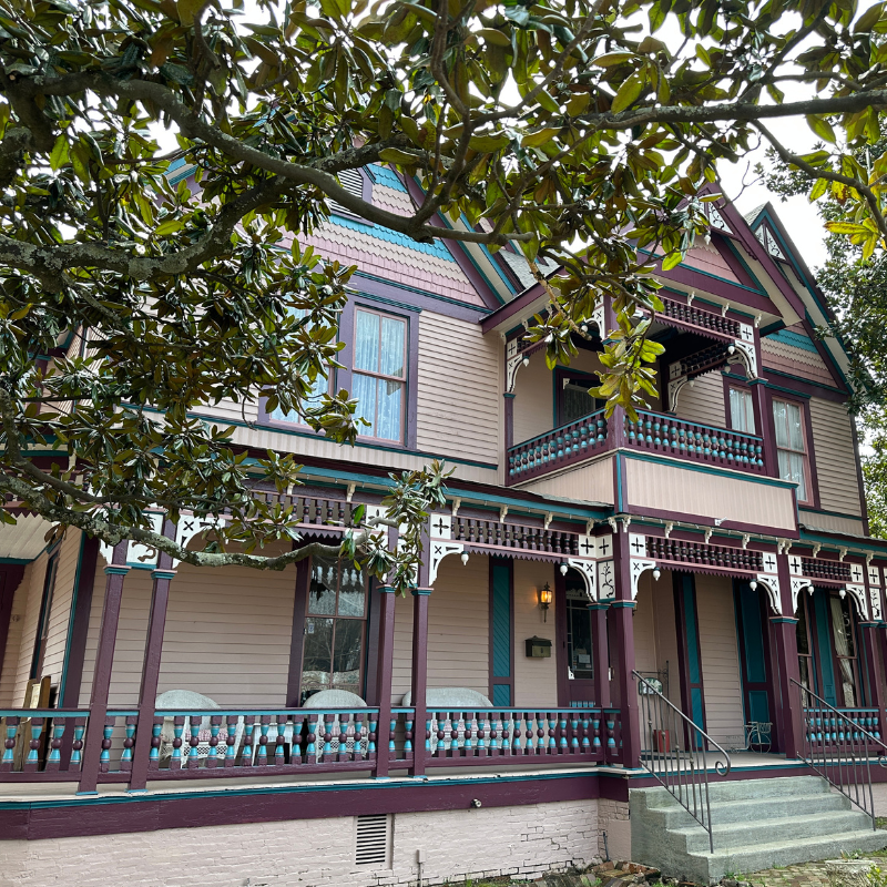 A two-story Victorian house with a wraparound porch, intricate wood trim, and a steep gabled roof is partially obscured by tree branches—an inviting glimpse into those eager to learn more about historic Acworth locations. A two-story Victorian house with a wraparound porch, intricate wood trim, and a steep gabled roof is partially obscured by tree branches—an inviting glimpse into those eager to learn more about historic Acworth locations.