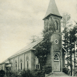 A black and white photo of a brick church with arched windows, a tall steeple, and ivy-covered front, surrounded by trees. Learn more about historic Acworth locations captured in timeless detail.