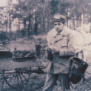 A man in an old-fashioned uniform stands beside a horse-drawn mail cart in a rural, wooded area—Learn More About Historic Acworth Locations as you step back in time.