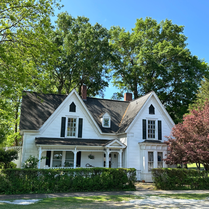 A white two-story Victorian-style house with black shutters, a front porch, and tall trees in the background on a sunny day. Learn more about historic Acworth locations like this beautiful home. A white two-story Victorian-style house with black shutters, a front porch, and tall trees in the background on a sunny day. Learn more about historic Acworth locations like this beautiful home.