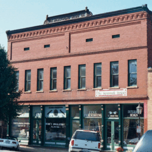 A two-story red brick building with businesses on the ground floor, including upholstery, interior design, and fine furnishing shops; a sign reads "DR ARMSTRONG BLOCK 06." Learn more about historic Acworth locations like this.