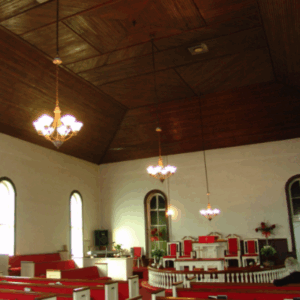 Interior of a church with wooden ceiling, chandeliers, red pews, arched windows, and a pulpit at the front. Learn More About Historic Acworth Locations as you explore this beautifully preserved sanctuary.