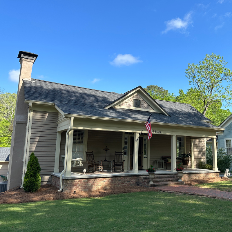 A single-story house with a covered front porch, rocking chairs, an American flag, brick steps, and a well-kept lawn under a clear blue sky. Learn more about historic Acworth locations like this charming home. A single-story house with a covered front porch, rocking chairs, an American flag, brick steps, and a well-kept lawn under a clear blue sky. Learn more about historic Acworth locations like this charming home.
