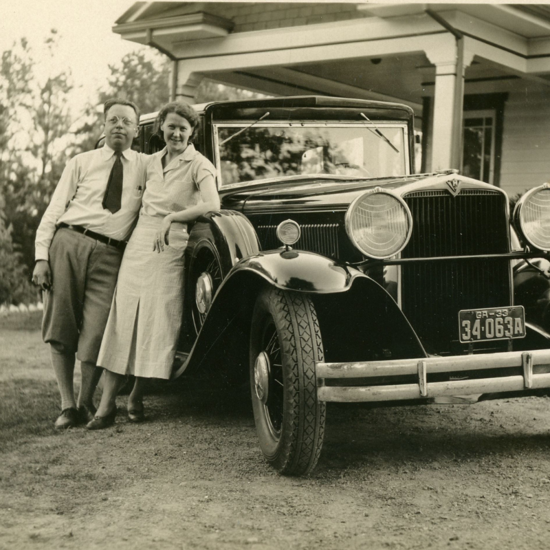 A man and woman stand together in front of a vintage car parked outside a house. The woman leans against the car while the man stands beside her, both facing the camera—capturing moments at one of many historic Acworth locations. Learn more about them today!. A man and woman stand together in front of a vintage car parked outside a house. The woman leans against the car while the man stands beside her, both facing the camera—capturing moments at one of many historic Acworth locations. Learn more about them today!.
