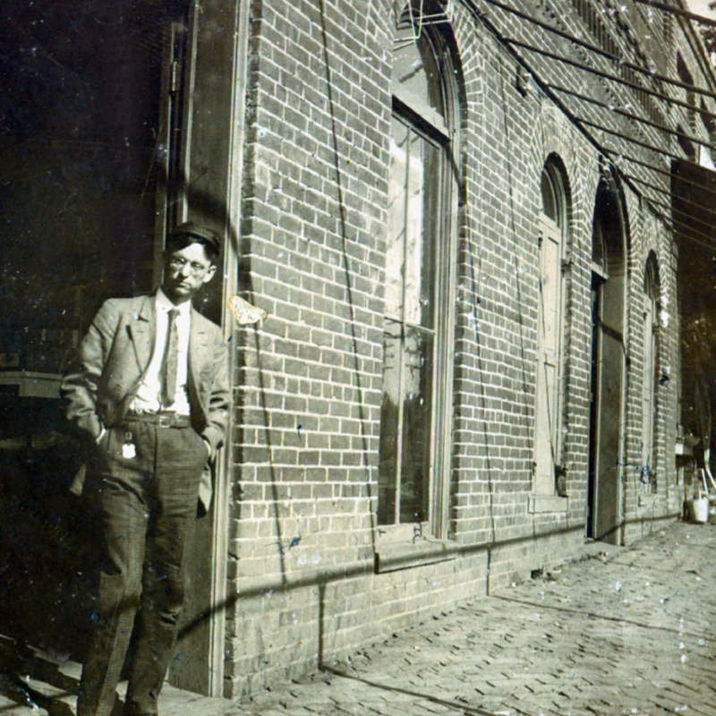 A man in a suit leans against a brick building with arched windows and doors on a cobblestone street. Learn more about historic Acworth locations as you take in the charm of this timeless setting. A man in a suit leans against a brick building with arched windows and doors on a cobblestone street. Learn more about historic Acworth locations as you take in the charm of this timeless setting.