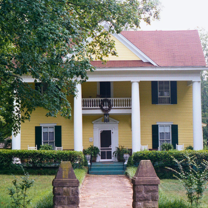 A two-story yellow house with white columns, green shutters, and a front porch, surrounded by trees and greenery—learn more about historic Acworth locations like this charming home. A two-story yellow house with white columns, green shutters, and a front porch, surrounded by trees and greenery—learn more about historic Acworth locations like this charming home.