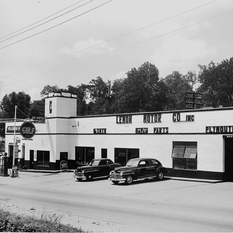 Black and white photo of a mid-20th-century car dealership with two parked cars, Gulf gas signage, De Soto and Plymouth vehicles, and a brick building surrounded by trees. Learn more about historic Acworth locations. Black and white photo of a mid-20th-century car dealership with two parked cars, Gulf gas signage, De Soto and Plymouth vehicles, and a brick building surrounded by trees. Learn more about historic Acworth locations.