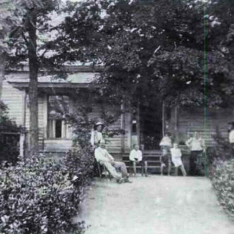 A group of people sit and stand on the front porch and walkway of a wooden house, surrounded by trees and shrubbery. Learn more about historic Acworth locations as you explore scenes like this from the past. A group of people sit and stand on the front porch and walkway of a wooden house, surrounded by trees and shrubbery. Learn more about historic Acworth locations as you explore scenes like this from the past.
