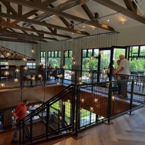 A modern, two-story café with large windows, hanging globe lights, wooden beams, and people talking and walking on the upper and lower levels—it’s the perfect spot to relax while exploring summer things to do in Acworth.