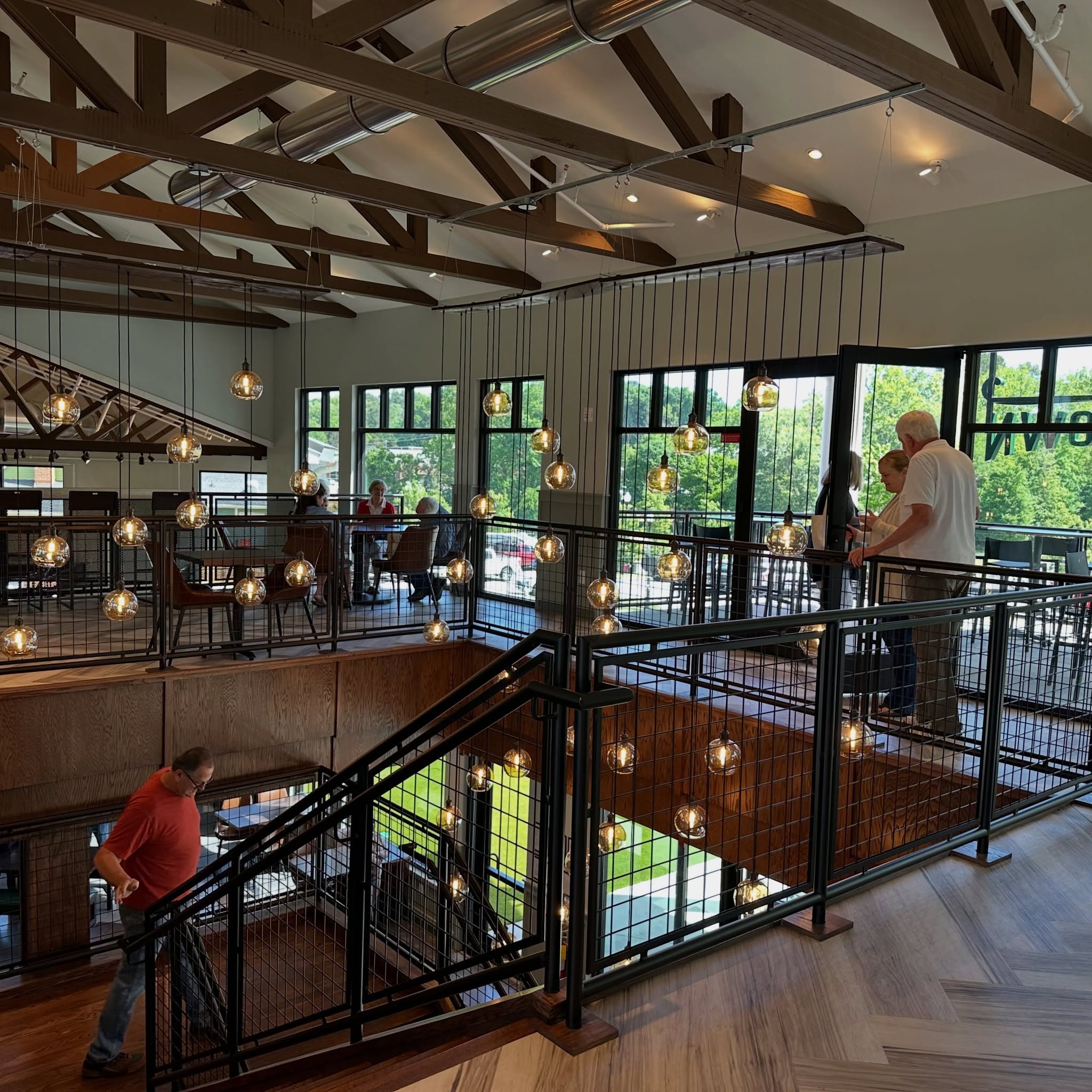 A modern, two-story café with large windows, hanging globe lights, wooden beams, and people talking and walking on the upper and lower levels—it’s the perfect spot to relax while exploring summer things to do in Acworth.