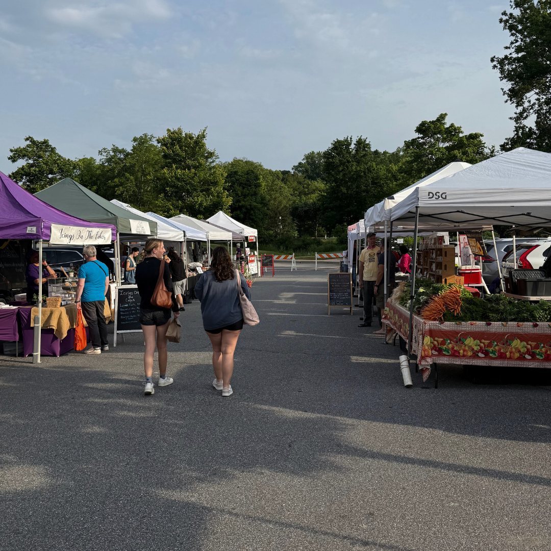 People walk between vendor tents at an outdoor farmers market on a sunny day, with produce and goods displayed on tables—a perfect addition to any end of summer bucket list. People walk between vendor tents at an outdoor farmers market on a sunny day, with produce and goods displayed on tables—a perfect addition to any end of summer bucket list.