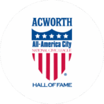 Logo for Acworth’s All-America City Hall of Fame, featuring a shield with stars and stripes and the text “National Civic League.”.