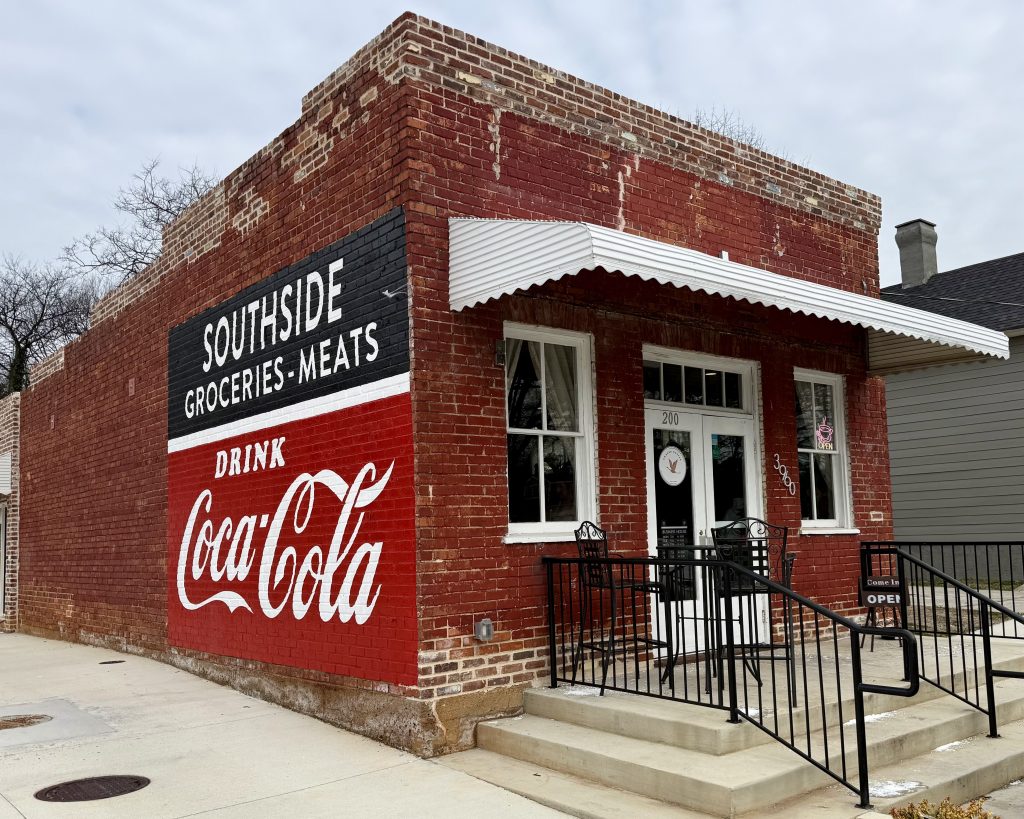 A small brick grocery store with a painted Coca-Cola advertisement on the side, labeled 