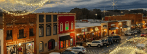 Welcome to Acworth, Georgia: A small town main street at dusk, with cars parked along storefronts decorated with holiday lights and sparkling overlays in the foreground and sky.