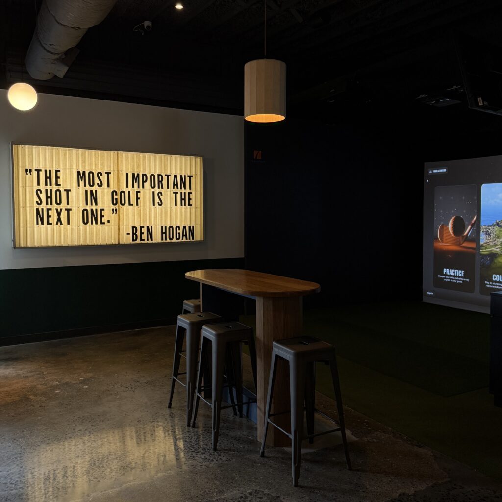 A dimly lit room with a wooden table and stools, a quote on the wall reads,