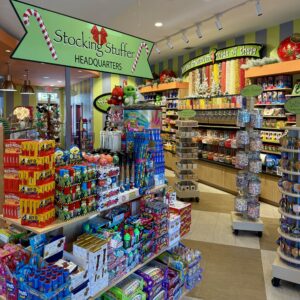 A brightly lit candy store interior with shelves of assorted sweets, boxed treats, and bins of bulk candy. Signs read "Stocking Stuffer Headquarters" and "Candy by the pound or piece." Your guide to Acworth gifts starts here!.