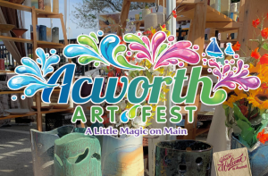 Colorful floral arrangements and artisan pottery are displayed outdoors behind a bold “Acworth Art Fest: A Little Magic on Main” event logo with bright design elements.
