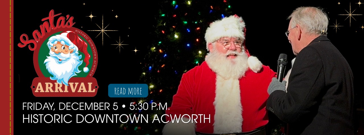 Santa Claus sits onstage next to a man holding a microphone during a holiday event in Historic Downtown Acworth, with event details displayed.