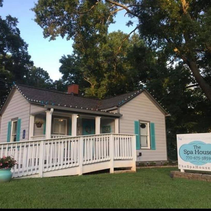 A small white house with teal shutters and a ramp, with a sign in front reading 