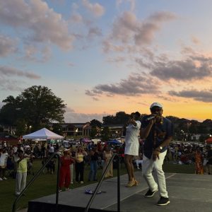 Two performers are on an outdoor stage at sunset, entertaining a large crowd at a festival with tents and event lighting in the background—one of the 26 Acworth-y Things to do in 2026 for an unforgettable evening.