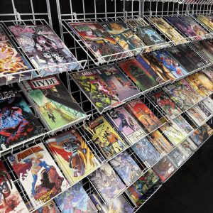Shelves displaying multiple rows of colorful comic books in protective sleeves, organized upright on white wire racks against a black background.