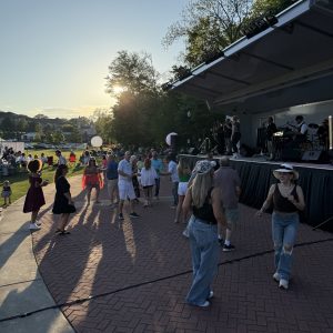 People dance in front of a stage with a live band performing outdoors in the early evening, sunlight streaming through the trees—a lively scene perfect for your list of 26 Acworth-y Things to do in 2026.