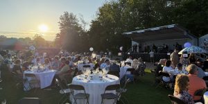 People sit at round tables on a lawn during an outdoor event at sunset, with a band performing on stage in the background—just one of the 26 Acworth-y Things to do in 2026.