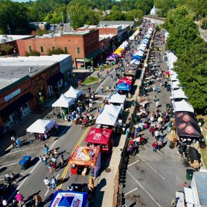 Aerial view of a street festival, part of the 26 Acworth-y Things to do in 2026, with rows of vendor tents, food stalls, and crowds enjoying a sunny day in a small town.
