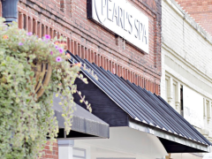 Pearls1 Brick storefront with a black awning and a sign reading "PEARL’S SPA"; a hanging planter with green foliage and pink flowers is visible on the left.