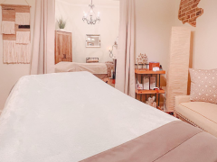 A neatly made massage table in a softly lit room with beige walls, decorative accents, and a small seating area.