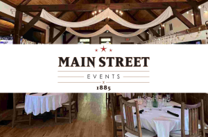 Interior of an event venue with round tables, wooden beams, draped white fabric, and the Main Street Events 1885 logo centered over the image.