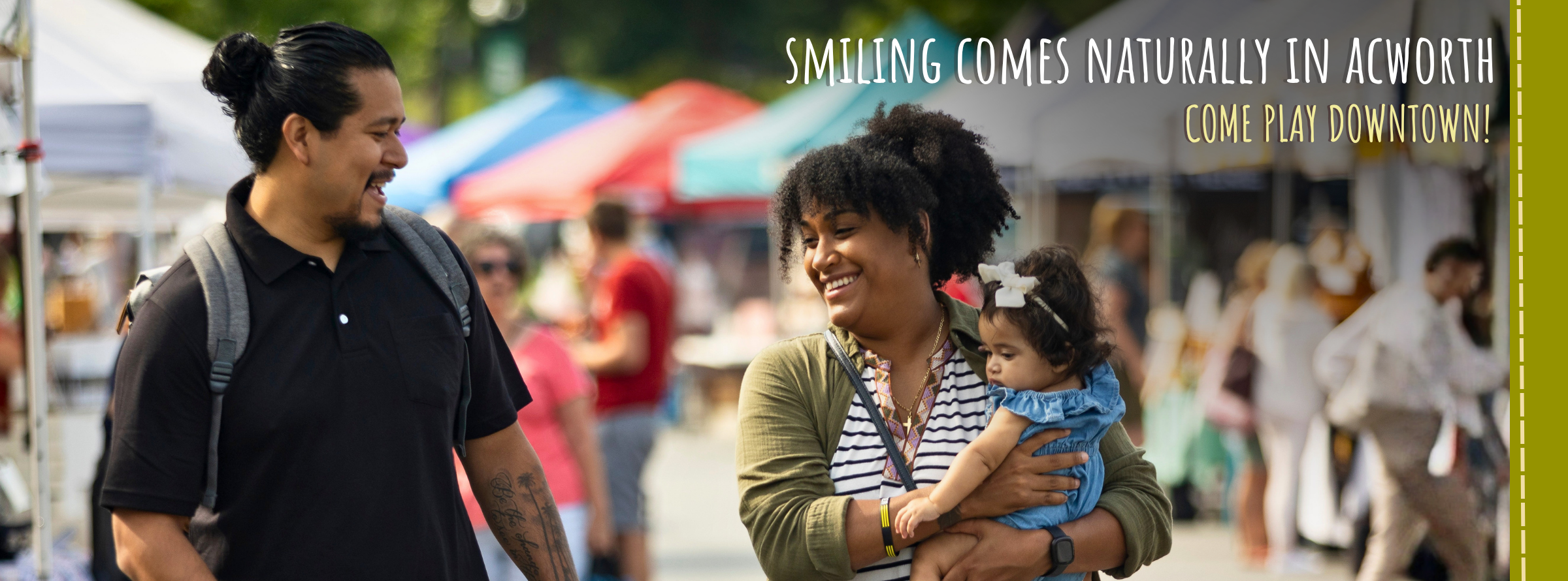 A man and woman walk outdoors at a market; the woman holds a baby. Text reads, "Smiling comes naturally in Acworth. Come play downtown!.