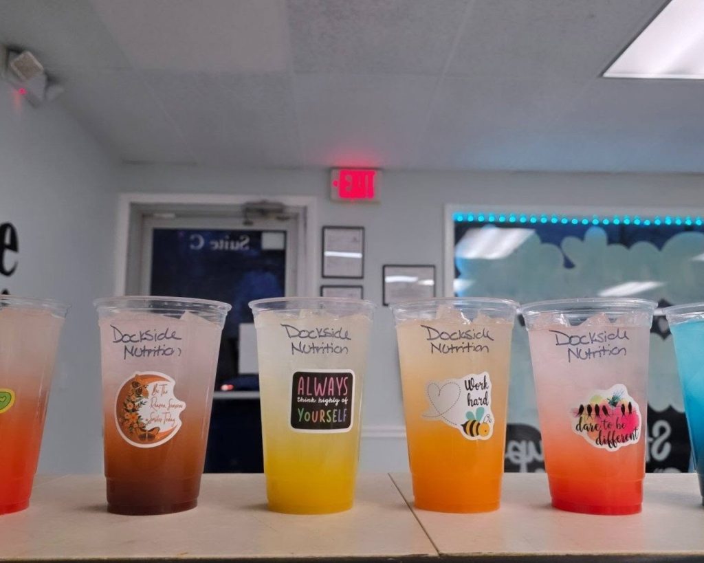 Five colorful drinks in clear plastic cups labeled 