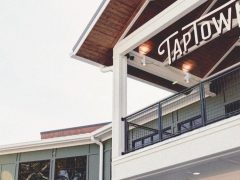 A partial view of a modern building with a balcony, railing, and a sign reading "TAPTOWN" mounted near the roof.