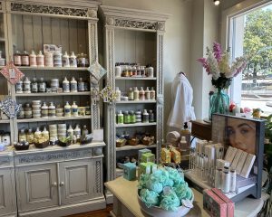 Shelves display bath and skincare products in Pearl's Spa in Downtown Acworth. A table holds toiletries, gift items, and a bowl of bath bombs while sunlight streams in through a window.