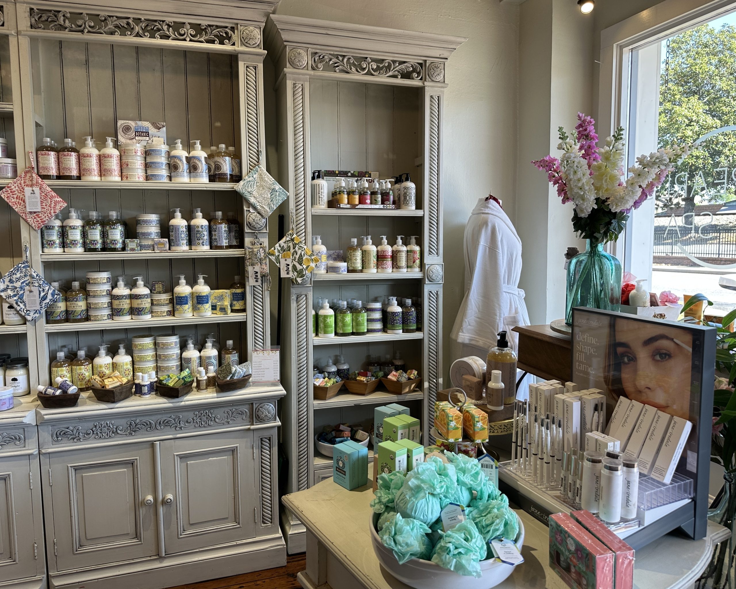 Shelves display bath and skincare products in Pearl's Spa in Downtown Acworth. A table holds toiletries, gift items, and a bowl of bath bombs while sunlight streams in through a window.